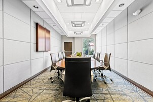 Un salón de conferencias con una larga mesa, sillas y vistas a un edificio a través de una ventana.