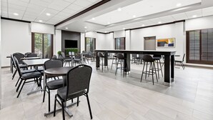 A modern conference room with multiple tables and chairs, recessed ceiling lights, and large windows with blinds.