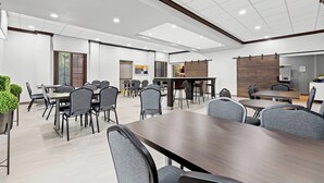 A modern dining area with multiple tables and chairs, a wooden accent wall, and recessed ceiling lights.