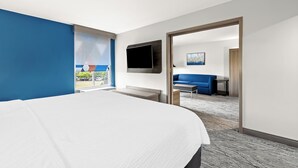 A modern hotel room with a large bed, a TV mounted on the wall, and a view of the outdoors through a window.