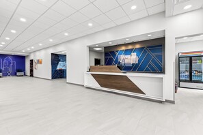 A modern reception area with a wooden counter, a blue and white geometric wall design, and a refrigerator with bottled water. - Holiday Inn Express Nashville-Hendersonville by IHG (Hendersonville)