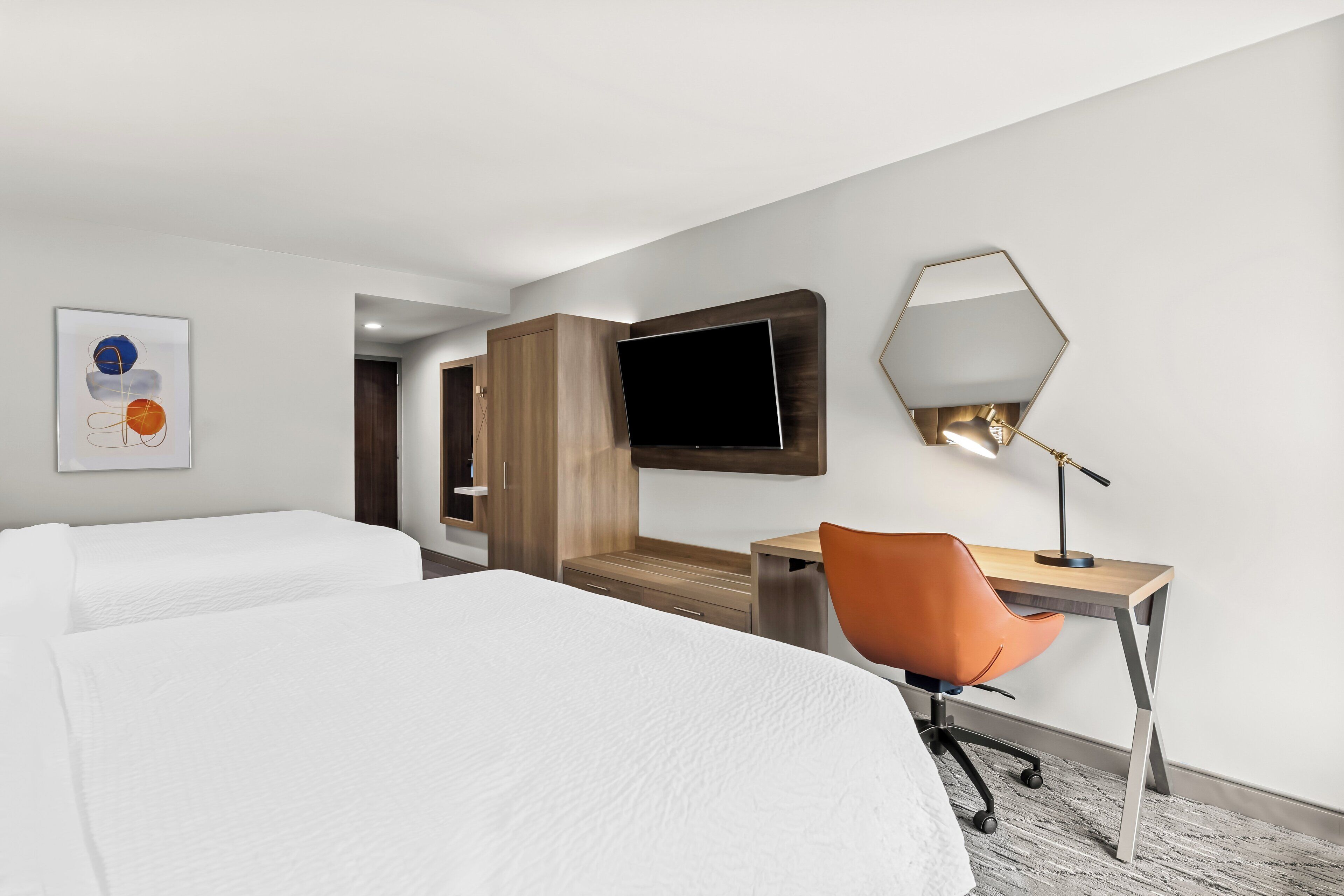 Une chambre d’hôtel avec deux lits, un bureau avec une chaise, une télévision et un miroir.