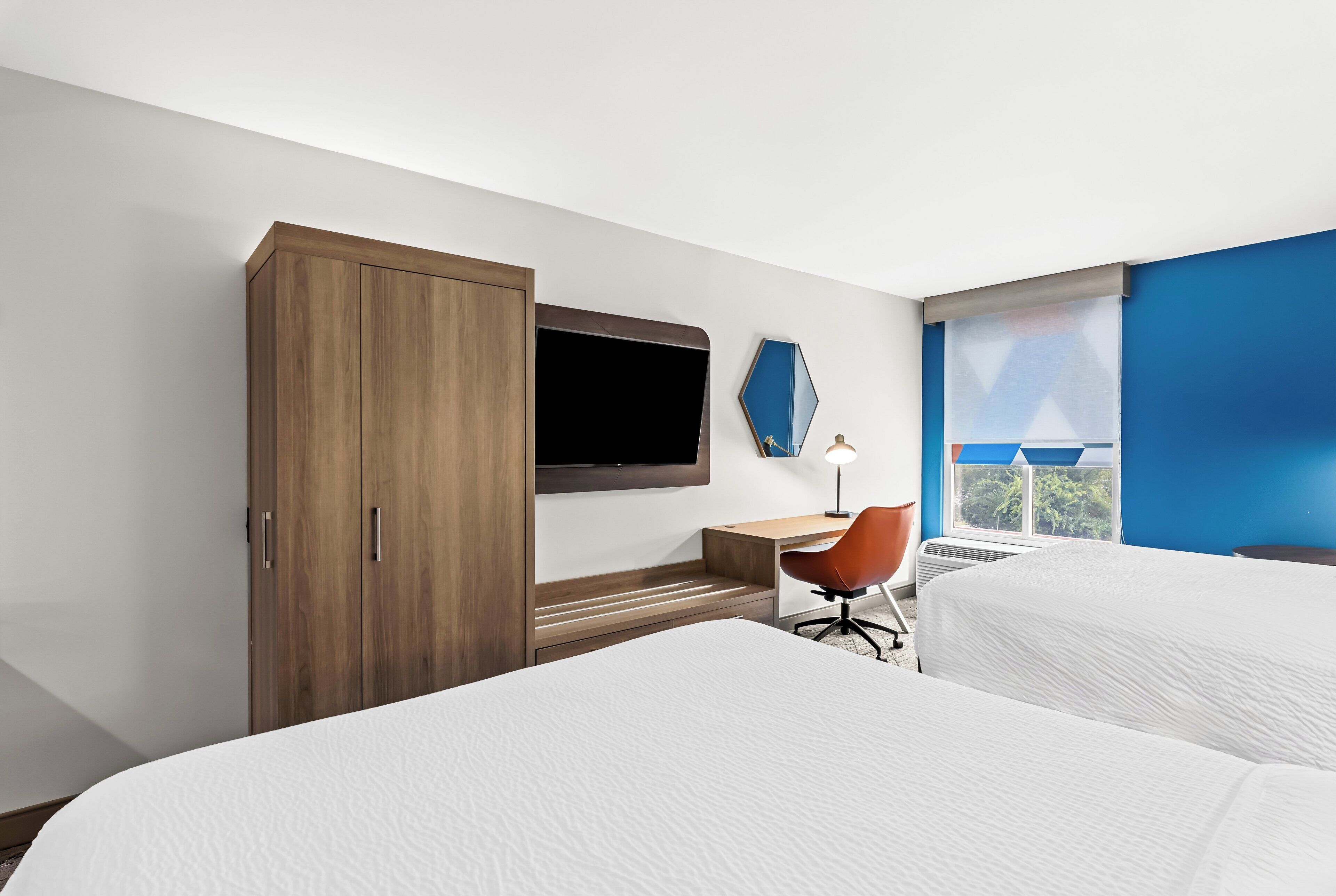 A hotel room with a bed, a desk with a chair, a TV, and a window with a view.