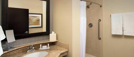 A bathroom with a granite sink, a mirror, a towel rack, and a shower area.
