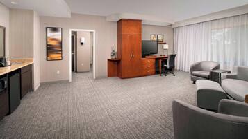 Hotelkamer met kitchenette, flatscreen-tv, bureau en zithoek met bank en fauteuils.