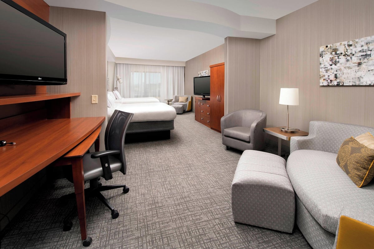 A hotel room with a bed, a desk with a chair, a sofa, a TV, and a lamp.