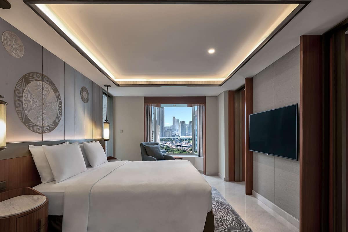 A modern hotel room with a large bed, a TV, and a city view.