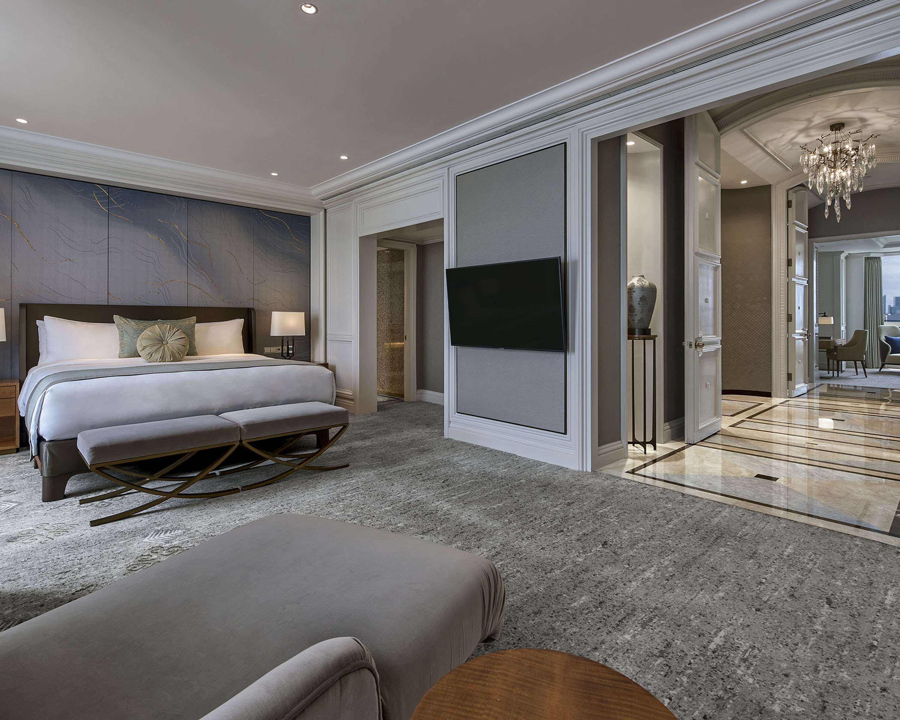Ein modernes Hotelzimmer mit einem großen Bett, einer Sitzecke, einem Fernseher und einem Badezimmer mit Glasdusche.