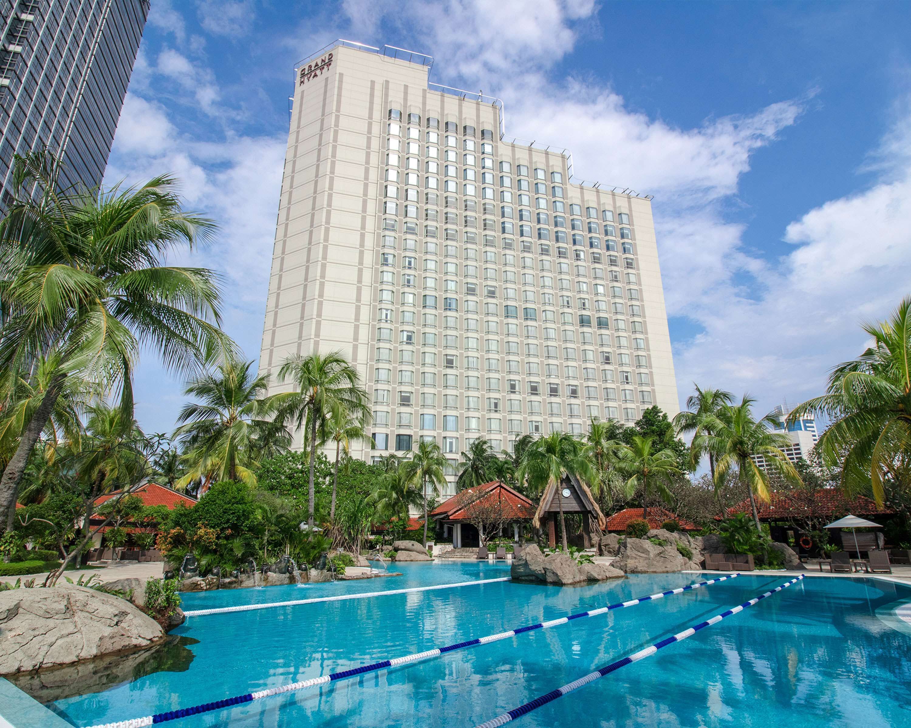 A hotel with a large swimming pool surrounded by palm trees and a clear blue sky.