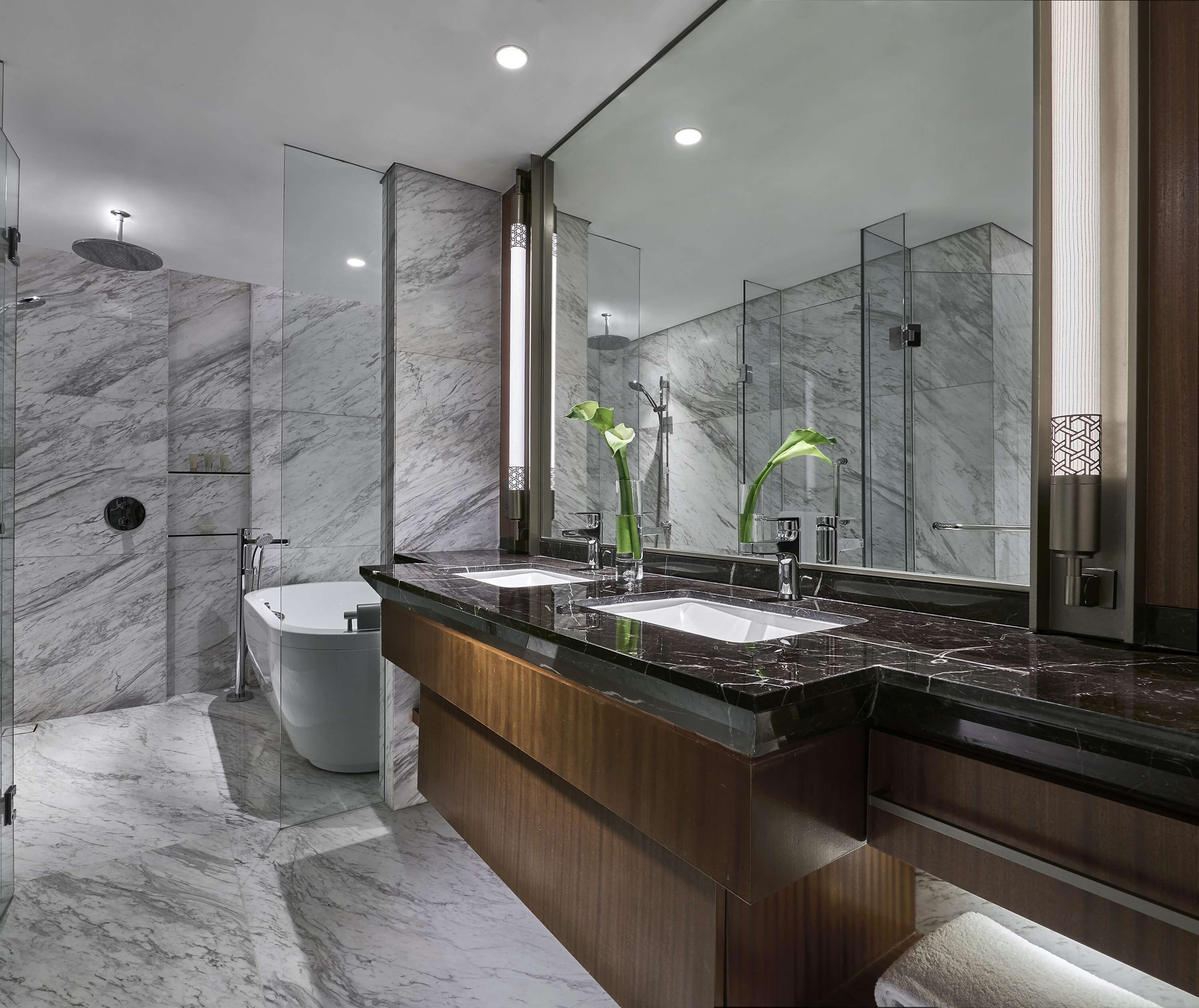 A modern bathroom with a marble floor, a freestanding bathtub, a large mirror, and a wooden vanity with two sinks.