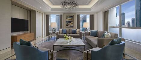 A spacious living room with a large flat-screen TV, comfortable seating, a chandelier, and a city view.