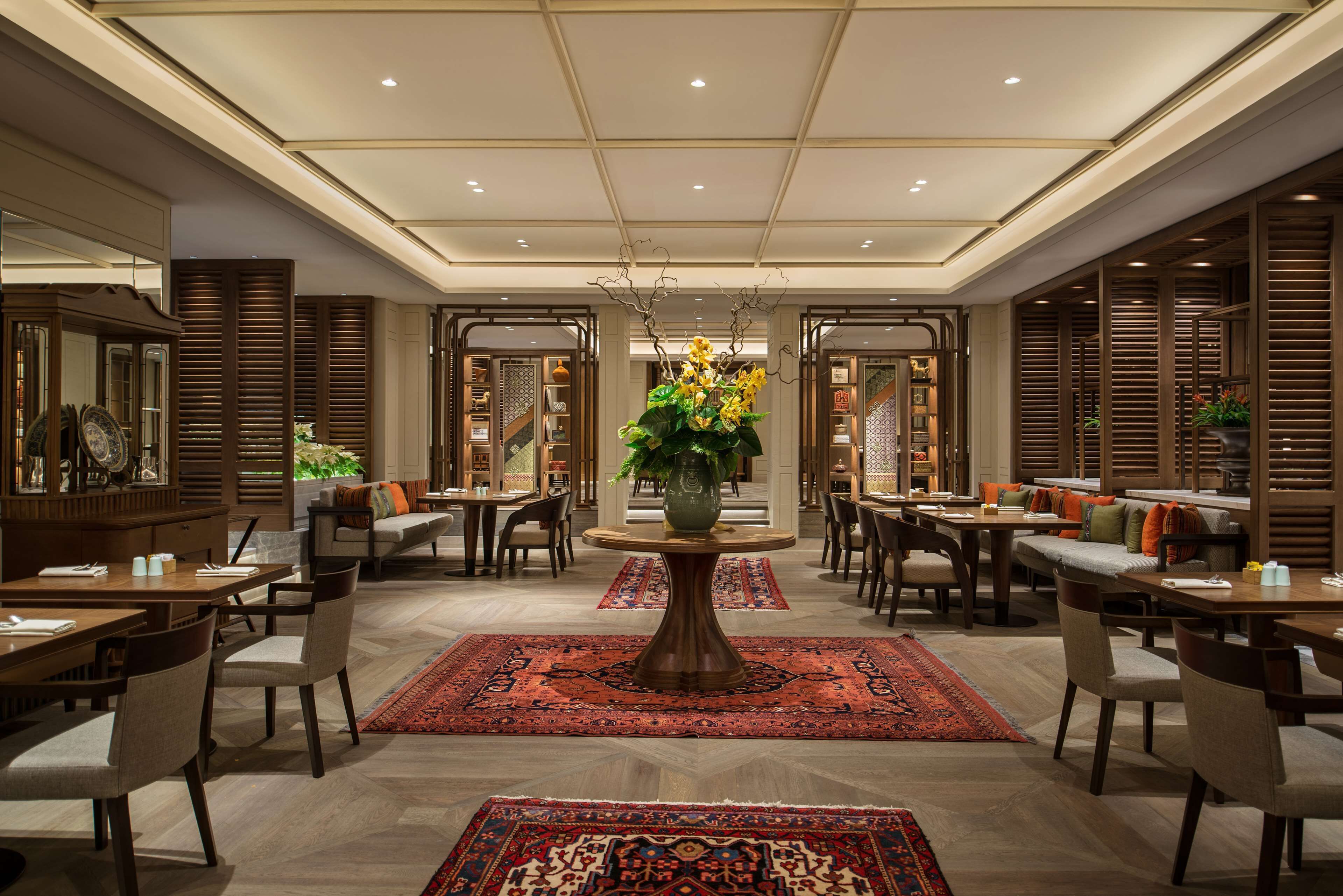Een ruime lobby met een centrale ronde tafel, verschillende zithoeken en een grote decoratieve vaas met bloemen.