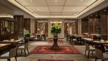 Een ruime lobby met een centrale ronde tafel, verschillende zithoeken en een grote decoratieve vaas met bloemen.