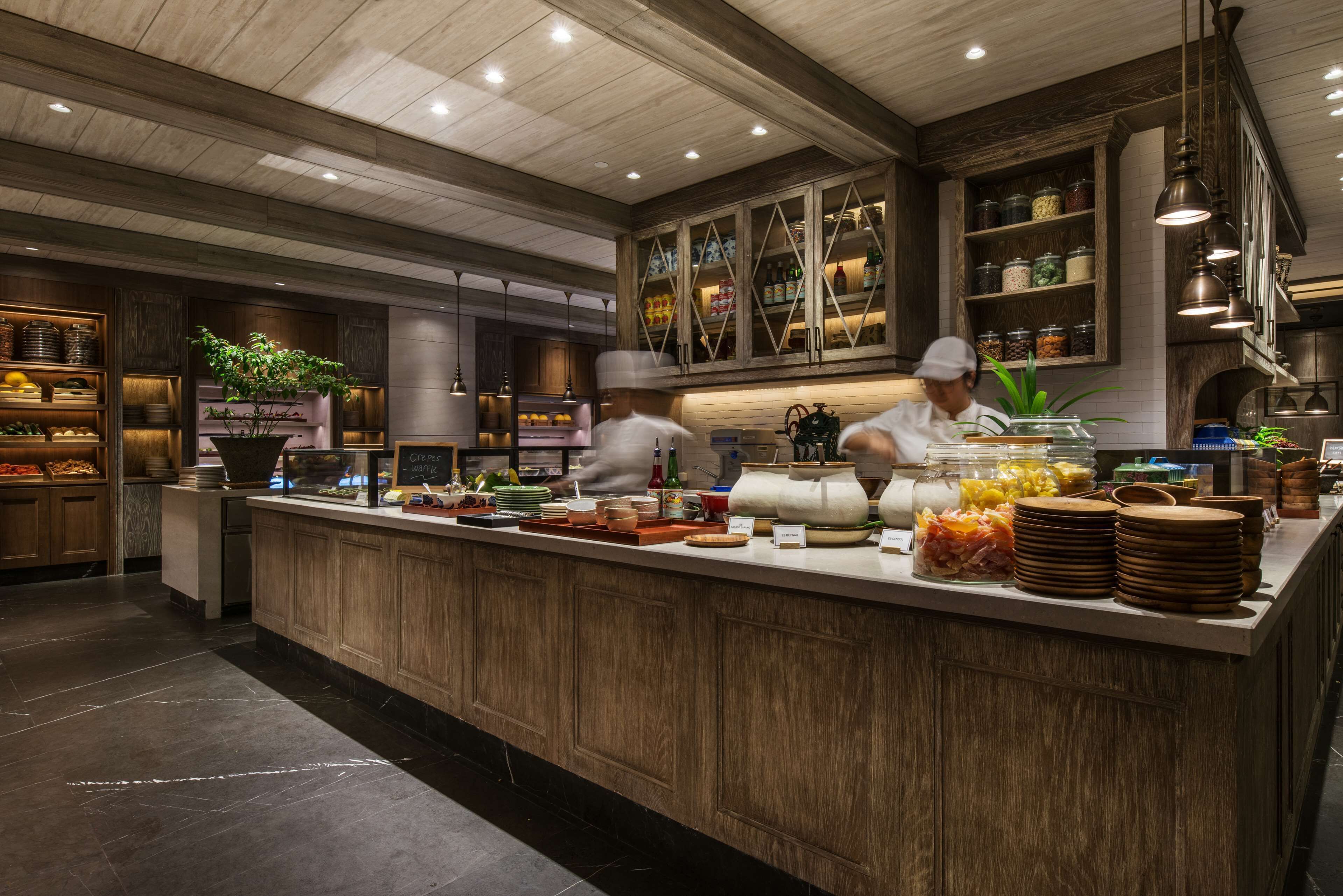 A modern kitchen with wooden cabinets, a marble countertop, and a chef preparing food.
