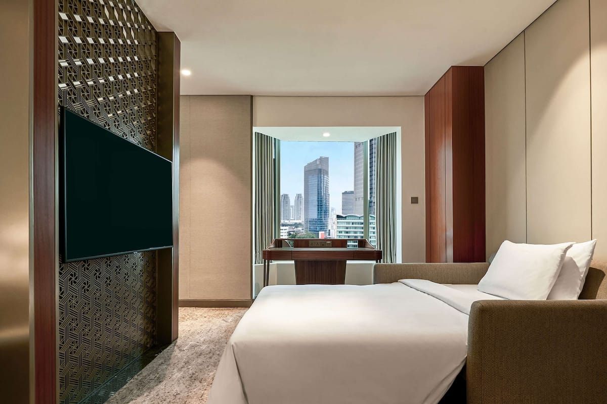 A hotel room with a large bed, a desk, and a view of city buildings.