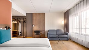 Et hotelværelse med seng, en grå sofa, et skrivebord med stol og et garderobeskab.