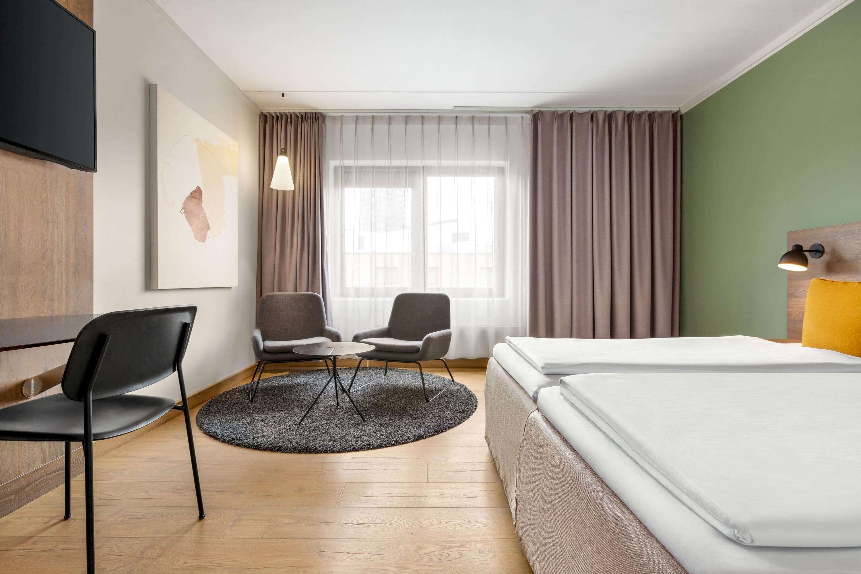 Una habitación de hotel con una cama, dos sillones, una mesita y un televisor montado en la pared.