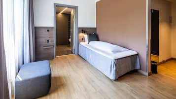 A modern hotel room with a single bed, a small seating area, and a bathroom visible through an open door.