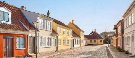 A cobblestone street lined with traditional European buildings, featuring uniform facades and pitched roofs.