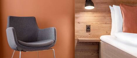 Une chambre moderne avec un fauteuil gris, une tête de lit en bois et une table de chevet avec une lampe.