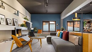 En moderne stue med sofa, stole, sofabord og pejs. Der er et bogreol med pynteting og et vindue med udsigt til en murstensbygning.