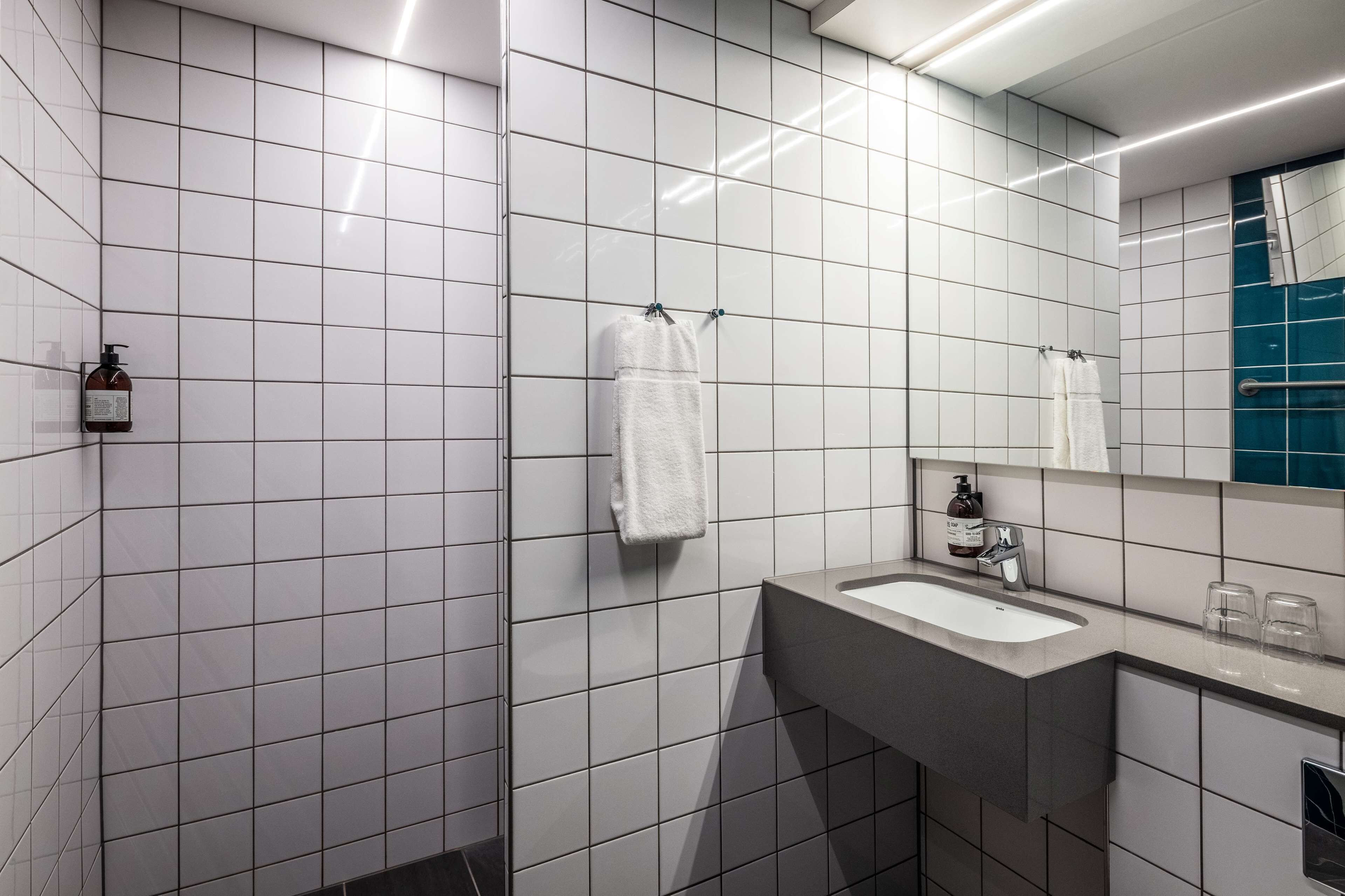 Un baño moderno con paredes de azulejos blancos, un lavamanos gris y un espejo encima.