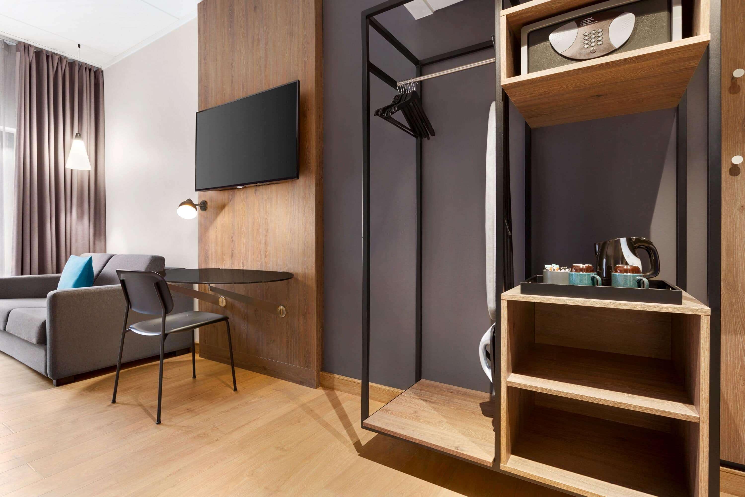 Una habitación de hotel moderna con una televisión de pantalla plana montada en la pared, un mueble de madera con microondas y una zona de estar con una mesa y sillas.
