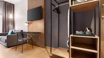 Una habitación de hotel moderna con una televisión de pantalla plana montada en la pared, un mueble de madera con microondas y una zona de estar con una mesa y sillas.