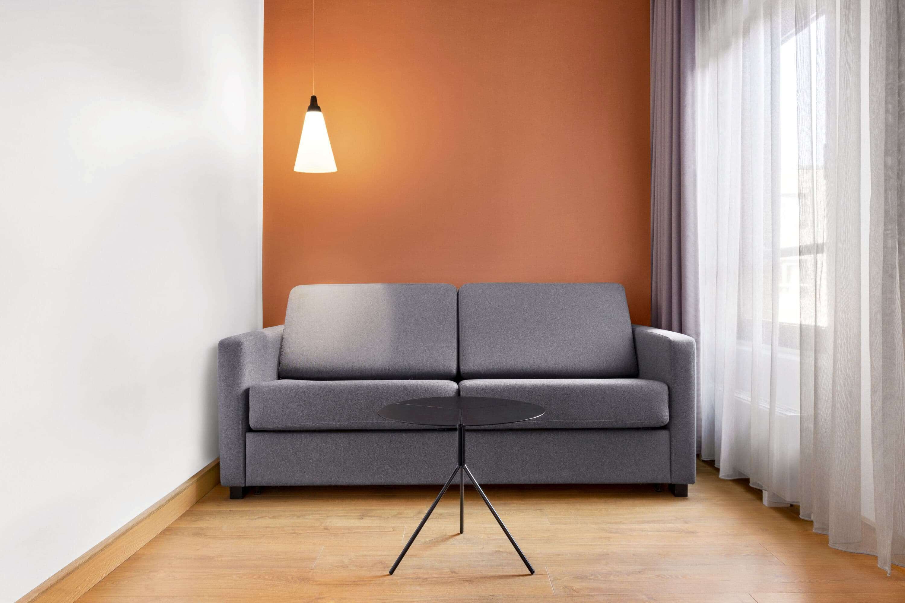 Una sala de estar moderna con un sofá gris, una mesa redonda negra con base de trípode y una lámpara colgante.