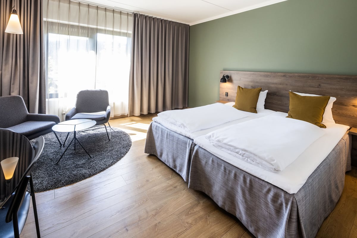 A hotel room with a large bed, two bedside tables, a chair, and a small table.