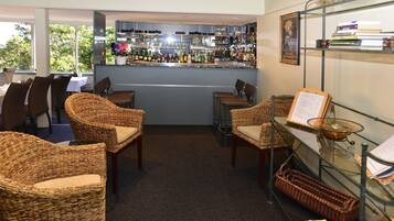 A bar area with wicker chairs, a glass table, and shelves with books and bottles.