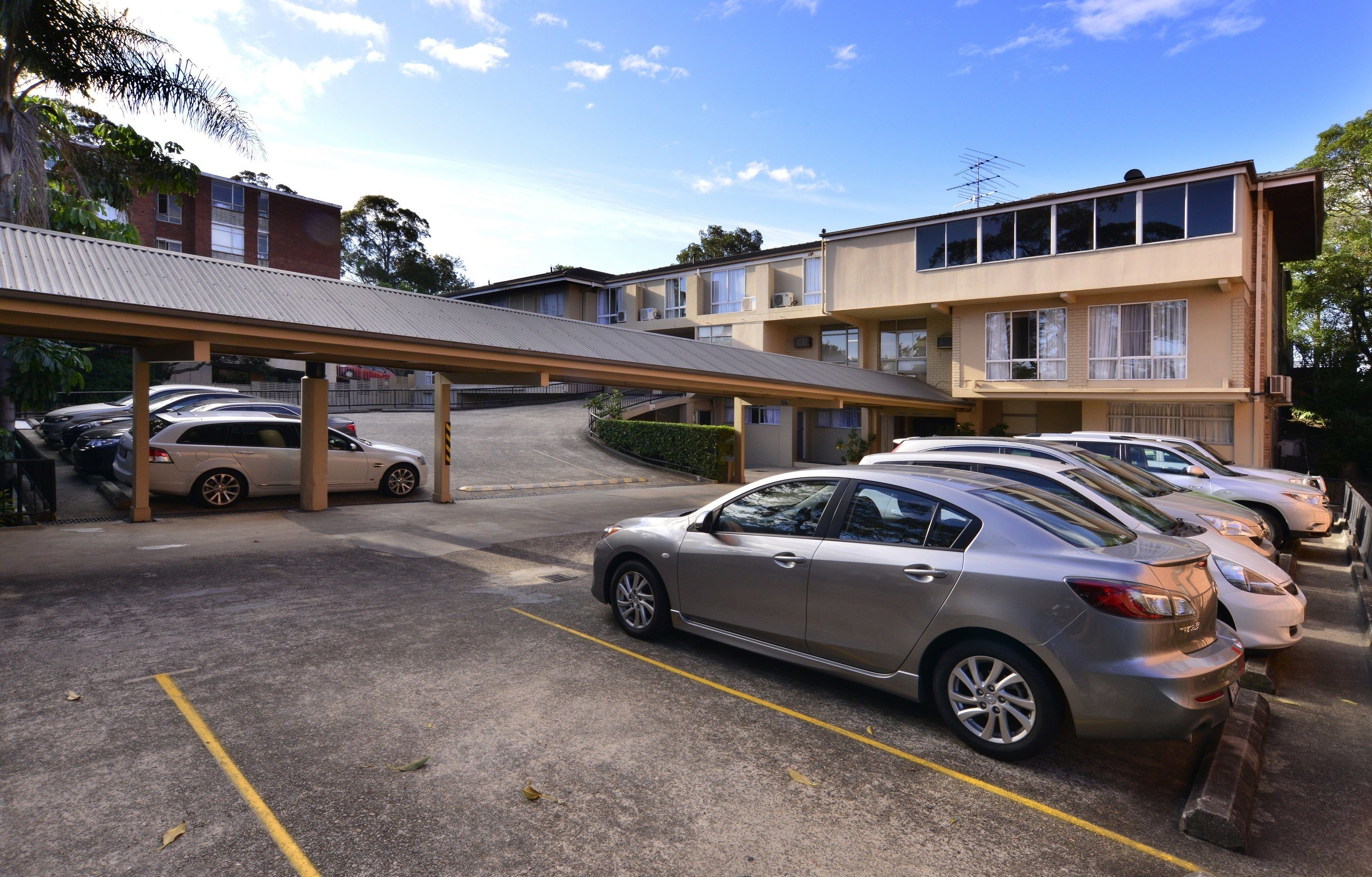 A parking lot with several cars, a covered walkway, and a building with multiple windows and balconies.