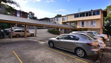 A parking lot with several cars, a covered walkway, and a building with multiple windows and balconies.