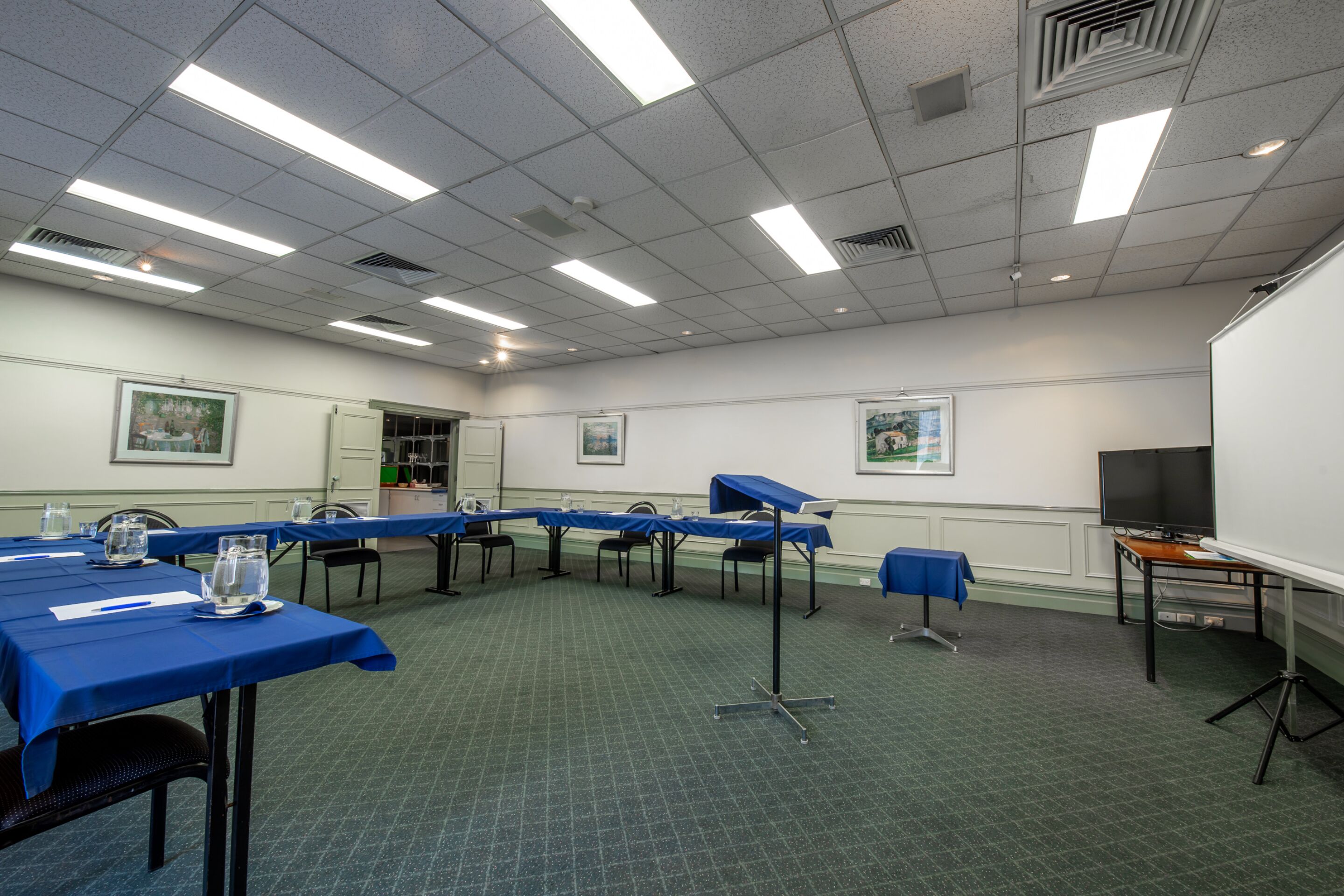 Une salle de conférence équipée de tables, de chaises, d’un projecteur et d’un tableau blanc.