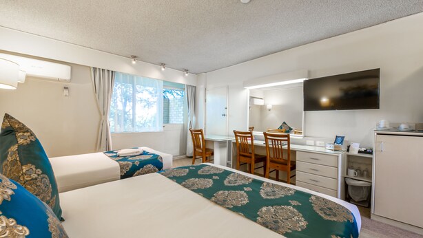Ein Hotelzimmer mit zwei Betten, einem Schreibtisch, einem Stuhl, einem Fernseher und einem Fenster mit Vorhängen.