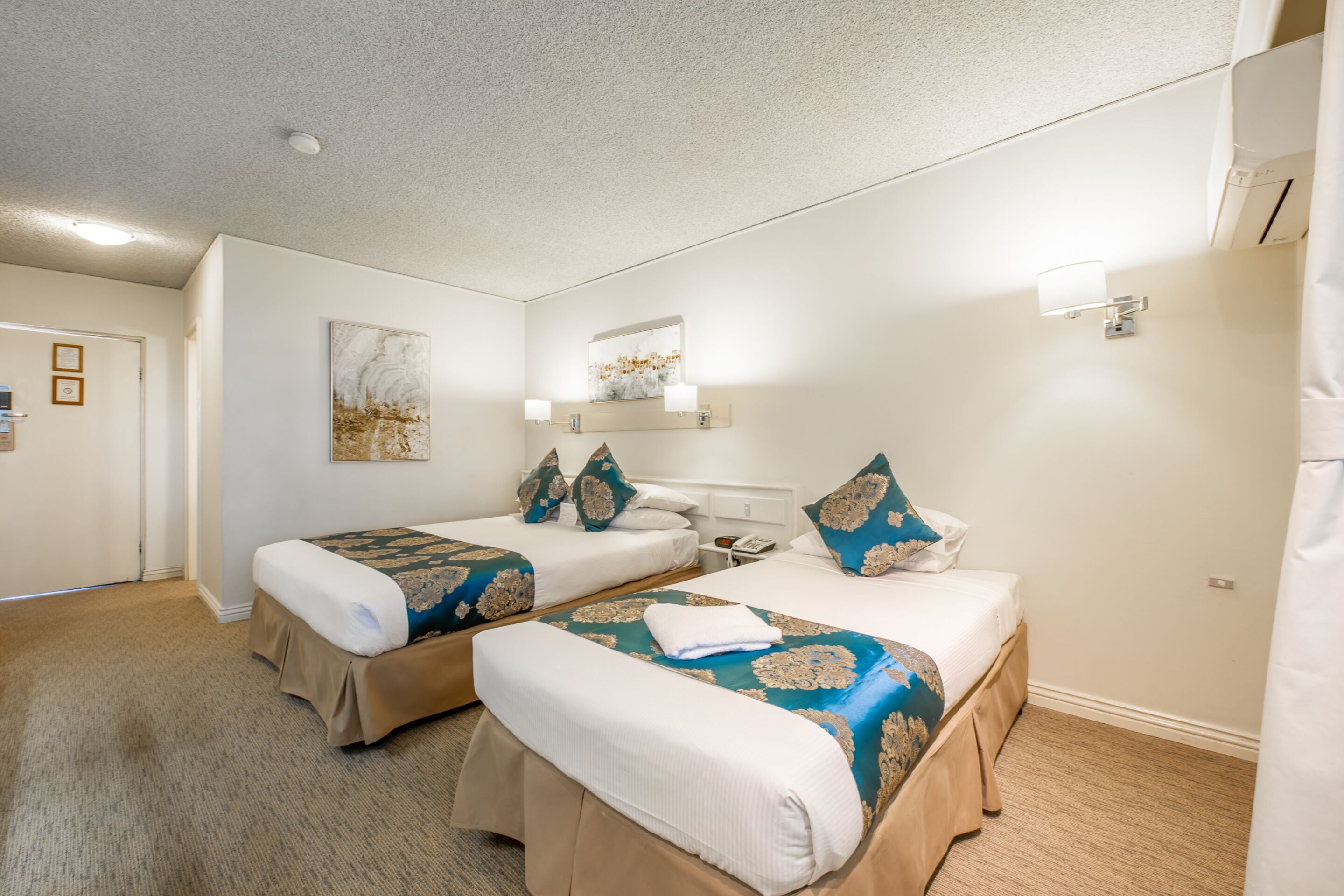 A hotel room with two beds, a bathroom, and a hallway.