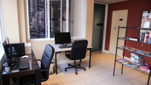 A workspace with two desks, computers, chairs, and a bookshelf with magazines. - Twin Towers Inn (Greenwich)