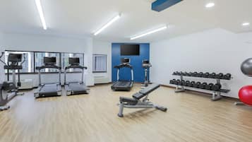 A gym with treadmills, a bench press, dumbbells, and a red exercise ball.