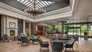 A spacious lobby with a high ceiling, a fireplace, modern seating, and large windows offering a view of greenery. - Four Points by Sheraton San Diego (San Diego)