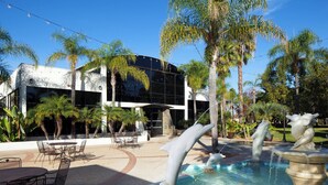 A modern building with a reflective glass facade, surrounded by palm trees and a pool with dolphin sculptures. - Four Points by Sheraton San Diego (San Diego)