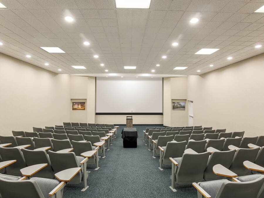 A conference room with rows of chairs, a projector screen, and a podium.