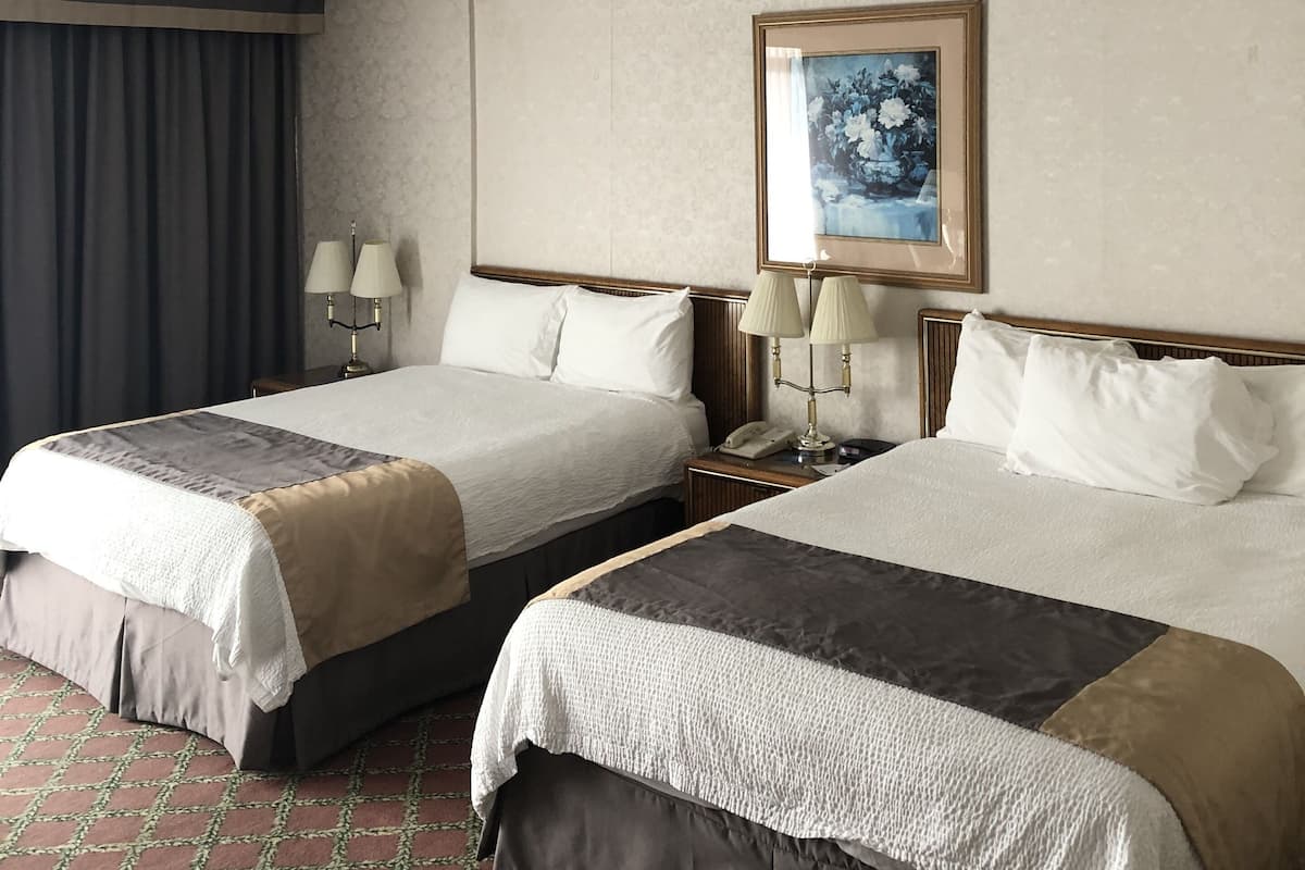 A hotel room with two beds, a patterned wall, a painting, and a patterned floor.