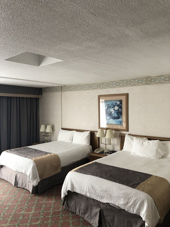 A hotel room with two beds, a patterned wall, a painting, and a patterned floor.