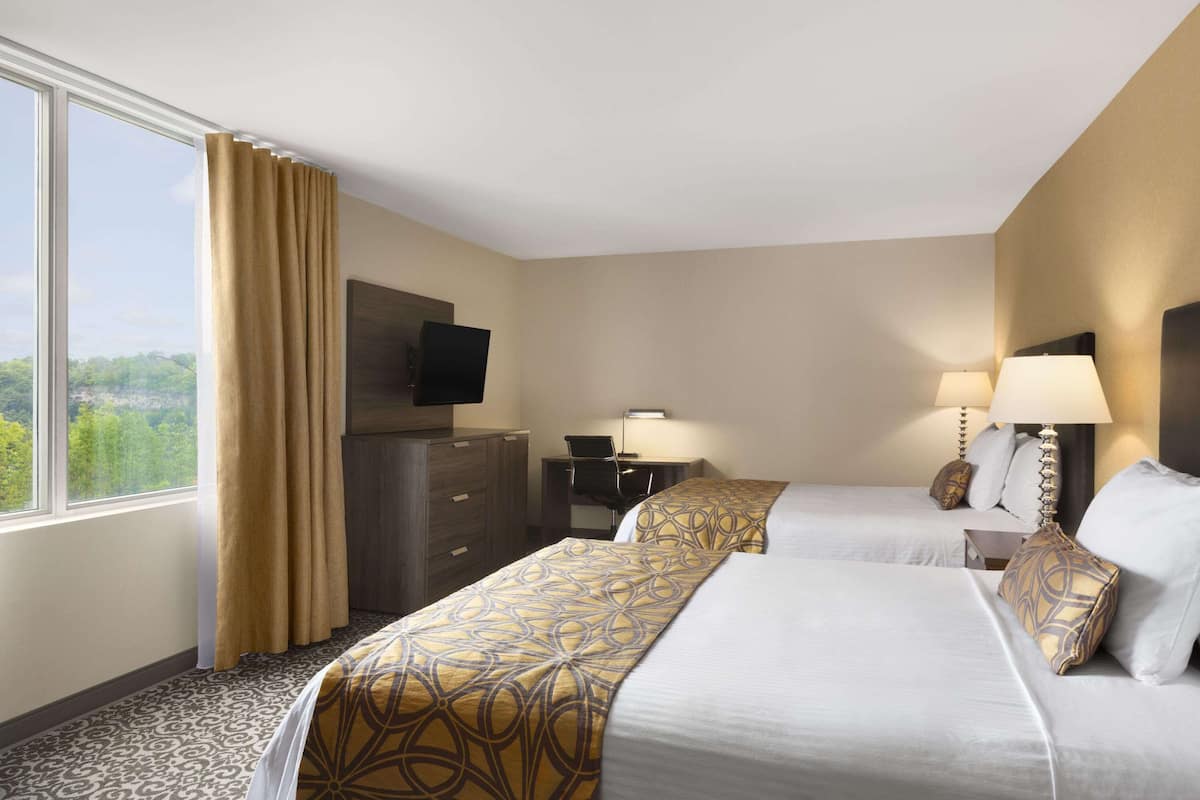A hotel room with two beds, a desk, a TV, and a window with curtains.