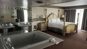 Habitación de hotel con una bañera grande, una cama con dosel, un tocador con espejo y una mesita de noche.