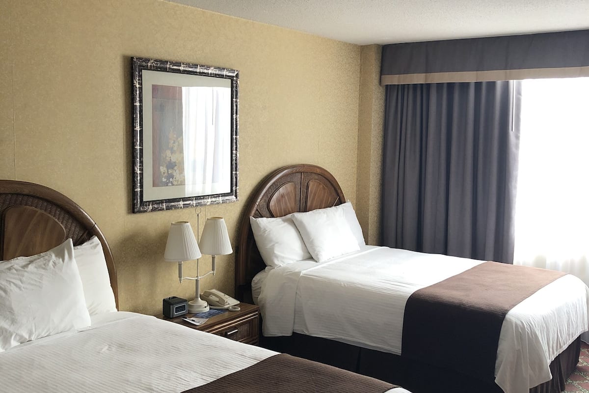 A hotel room with two beds, a nightstand with a lamp, a telephone, and a framed picture on the wall.