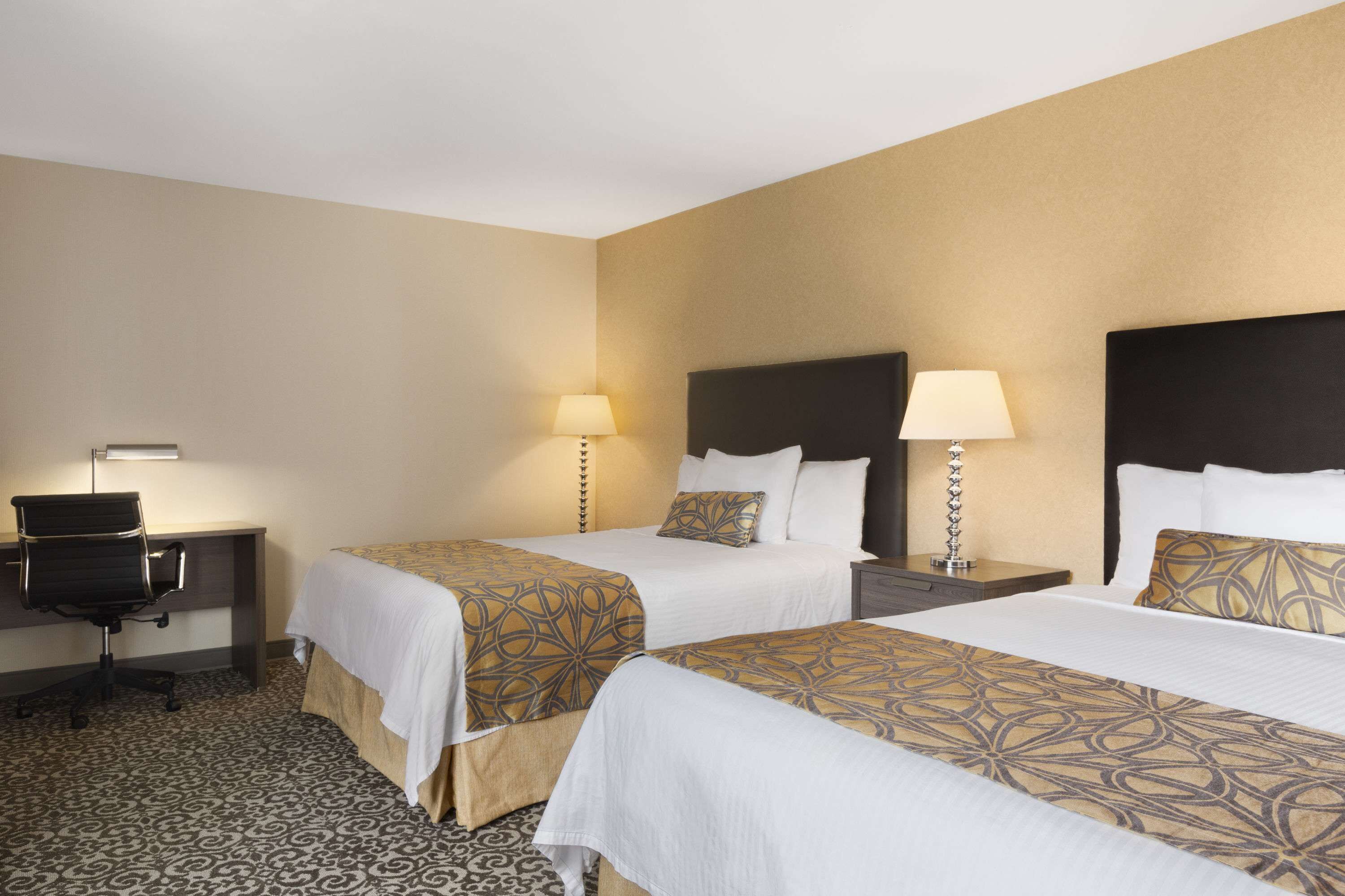 A hotel room with two beds, a desk, and a chair.
