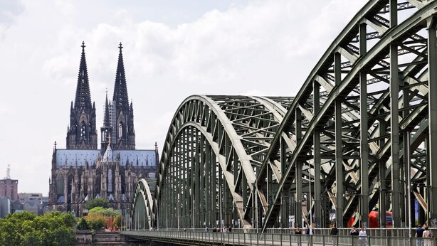 Een grote stalen brug met een gotische kathedraal op de achtergrond.
