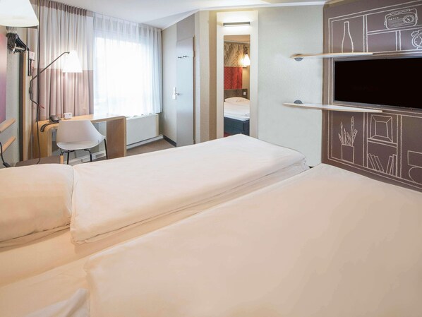 A hotel room with two beds, a desk, a chair, a TV, and a bathroom visible through an open door.