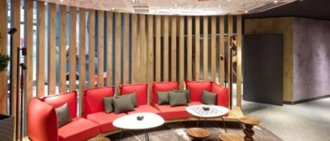 Un espace de détente moderne avec un canapé rouge, des tables rondes en bois et des lambris en bois verticaux.